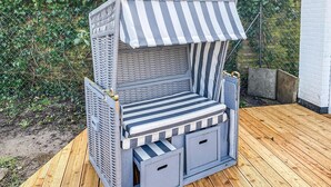 Un petit espace extérieur aménagé avec des sièges, délimité et abrité par un auvent à rayures, comprenant un banc rembourré et des compartiments de rangement.