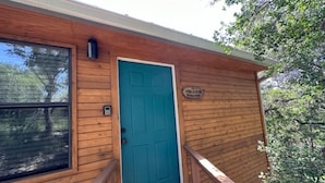 Una cabaña de madera con una puerta azul turquesa, una ventana y un pequeño letrero en la pared.