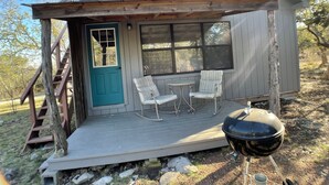 A cabin with a porch, two chairs, a grill, and a blue door. - Relaxing Getaway at The Siesta Cabin, Pet Friendly (Fredericksburg)