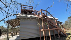 A rustic cabin with a wooden deck and a staircase leading to a loft area. - Relaxing Getaway at The Siesta Cabin, Pet Friendly (Fredericksburg)