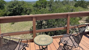 Une terrasse en bois avec une rambarde en métal, une petite table ronde et deux chaises en métal.