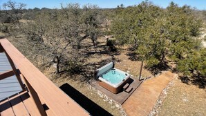 Un bain à remous entouré d’une terrasse en bois, offrant une vue sur un paysage aride et boisé.