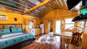 Un chalet confortable avec un intérieur en bois, un lit recouvert d’une couverture à motifs, un coin cuisine et une table à manger.