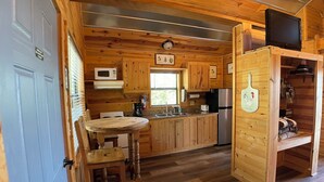 A wooden cabin interior with a kitchen area, a dining table, and a television.