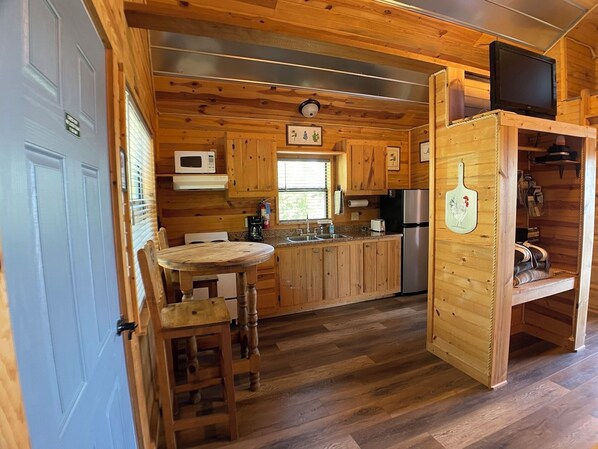 A wooden cabin interior with a kitchen area, a dining table, and a television.