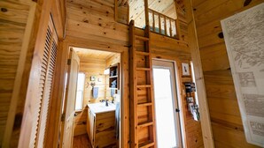 A wooden cabin interior with a loft bedroom, a staircase, and a bathroom.
