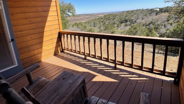 A wooden deck with a railing, a bench, and a view of a hilly landscape.