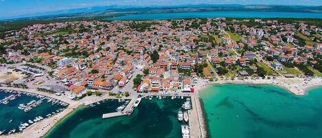 Vista aèria d'una població costanera amb un port esportiu, edificis residencials i una platja.