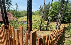 A wooden fence with a view of a house and a pool in a forested area.