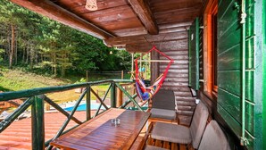 Una cabaña de madera con terraza, una hamaca y una mesa con sillas.