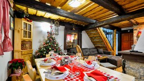 Un comedor con mesa de madera dispuesta para cuatro personas, un árbol de Navidad y un interior acogedor con vigas de madera a la vista.