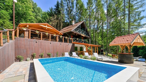 Un área de piscina con muelle de madera, sillas de descanso y un edificio de estilo rústico de cabaña con techo rojo.