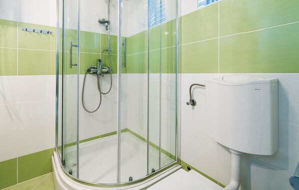Una ducha con cerramiento de vidrio, cabezal de ducha de mano y llave en la pared.
