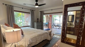Un dormitorio con cama, mesita de noche, lámpara y vistas al balcón exterior.