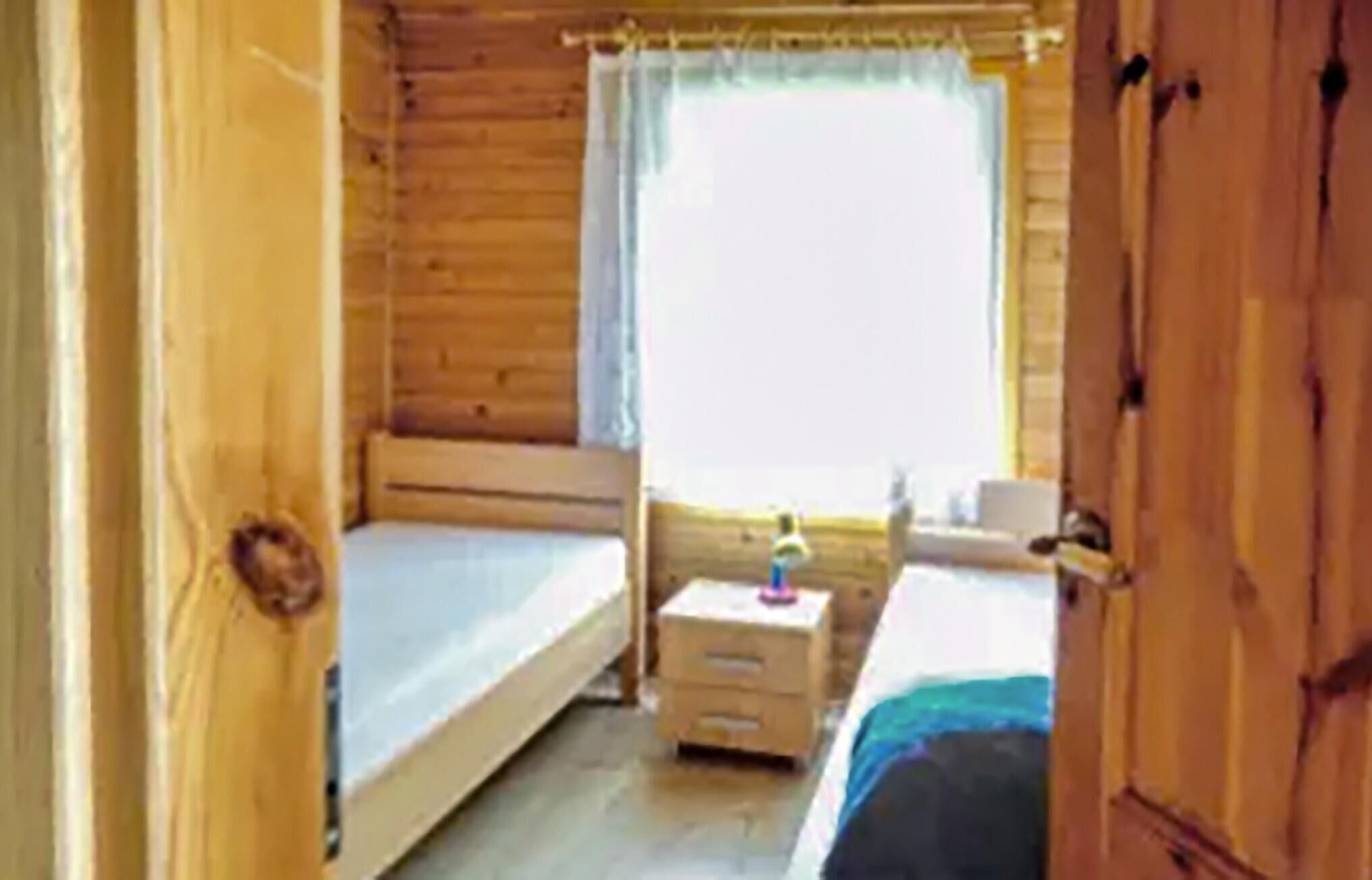 Una habitación de cabaña de madera con dos camas, una mesita y una ventana con cortinas.