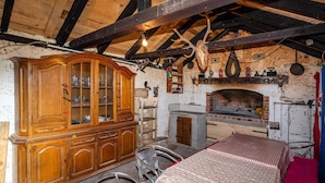 Une pièce rustique avec un meuble en bois, une chaise en métal, une nappe à motifs, une cheminée et divers objets de décoration.