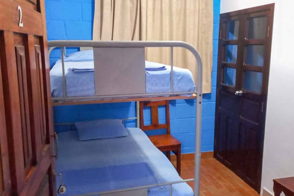 Une chambre avec un lit superposé, une porte en bois et un mur bleu.
