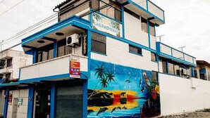 Un edificio con un mural de fauna marina y palmeras, un letrero que dice 'Hotel Las Palmeras', y una puerta de garaje cerrada.