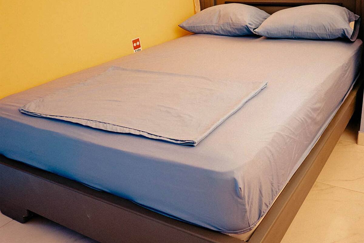 Une chambre avec un lit simple, une tête de lit en bois, une couvre-lit bleue et deux oreillers.
