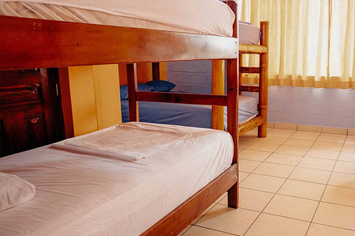 Une chambre avec un lit superposé, une structure en bois, un sol carrelé et une fenêtre avec des rideaux.