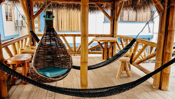 Una silla hamaca colgada de una estructura de bambú con vista al océano.
