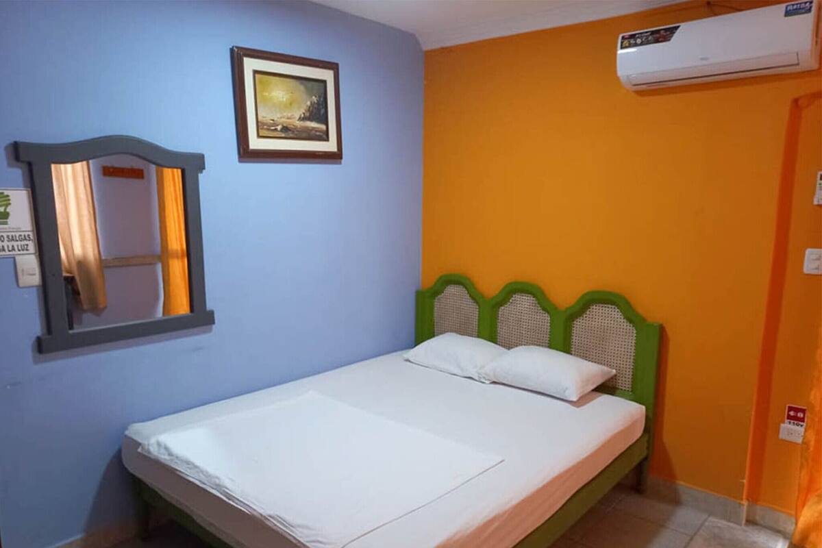 Un lit simple avec une tête de lit verte, un tableau encadré accroché au mur et un appareil de climatisation placé au-dessus.