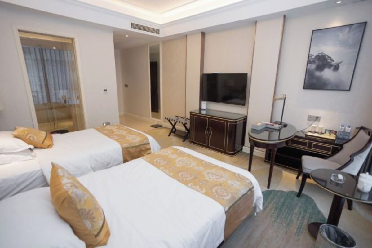 A hotel room with two beds, a desk, a chair, a TV, and a painting on the wall.