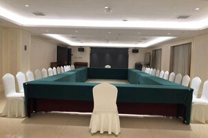 Un salón de conferencias con una mesa larga, sillas blancas y una silla blanca en primer plano.