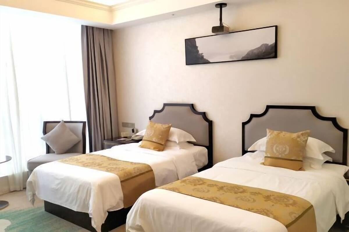 A hotel room with two beds, each with a headboard, a nightstand, a lamp, and a window with curtains.