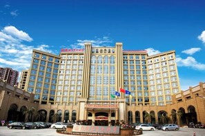A large hotel with a central entrance, multiple floors, and a courtyard with cars and palm trees. - Anfu Jiangjing Hotel (Anfu)