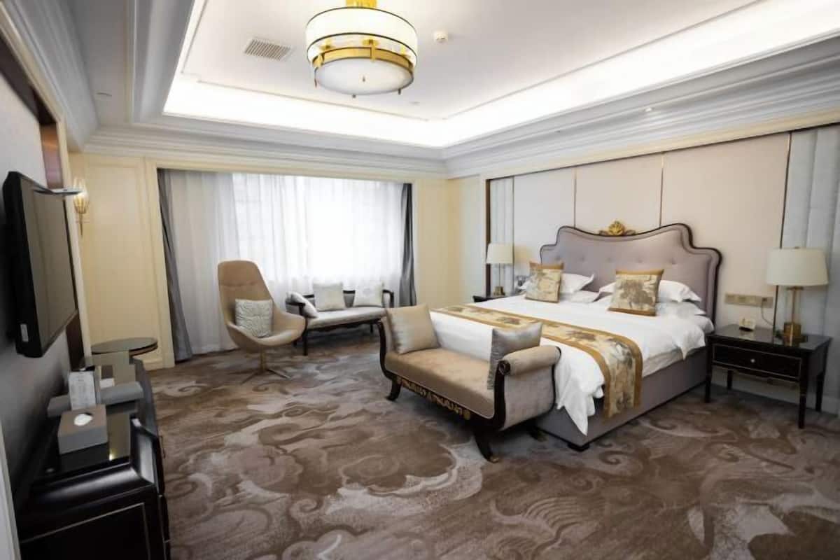 A hotel room with a large bed, a sofa, a chair, a desk, and a TV.