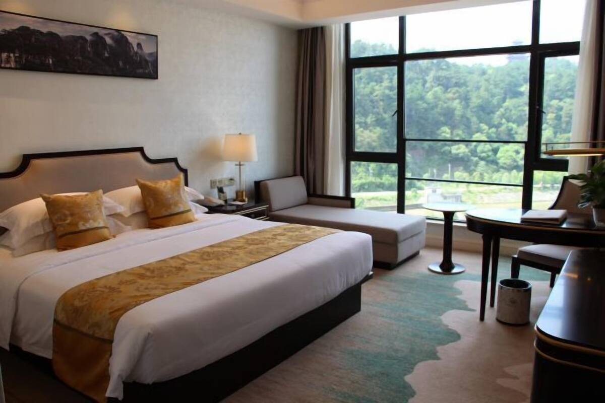 A hotel room with a large bed, a sofa, a desk, and a view of the outdoors.
