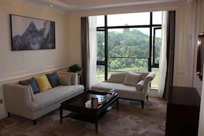 Una sala de estar con sofá, sillón, mesa de centro y un ventanal con vistas a zonas verdes.