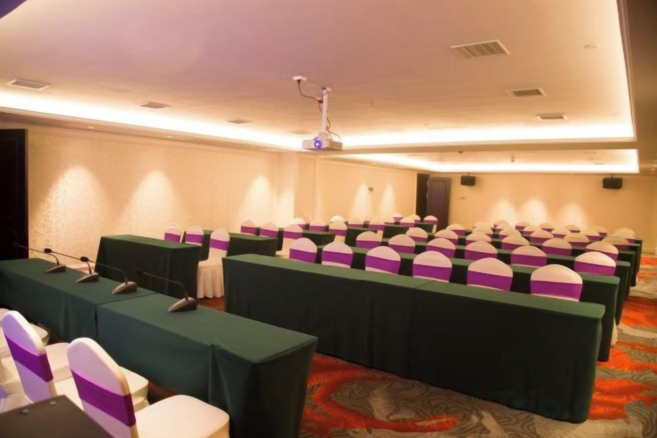 A conference room with rows of tables, each with a microphone and a laptop, and a projector mounted on the ceiling.