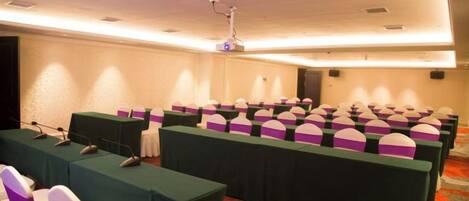 A conference room with rows of tables, each with a microphone and a laptop, and a projector mounted on the ceiling.