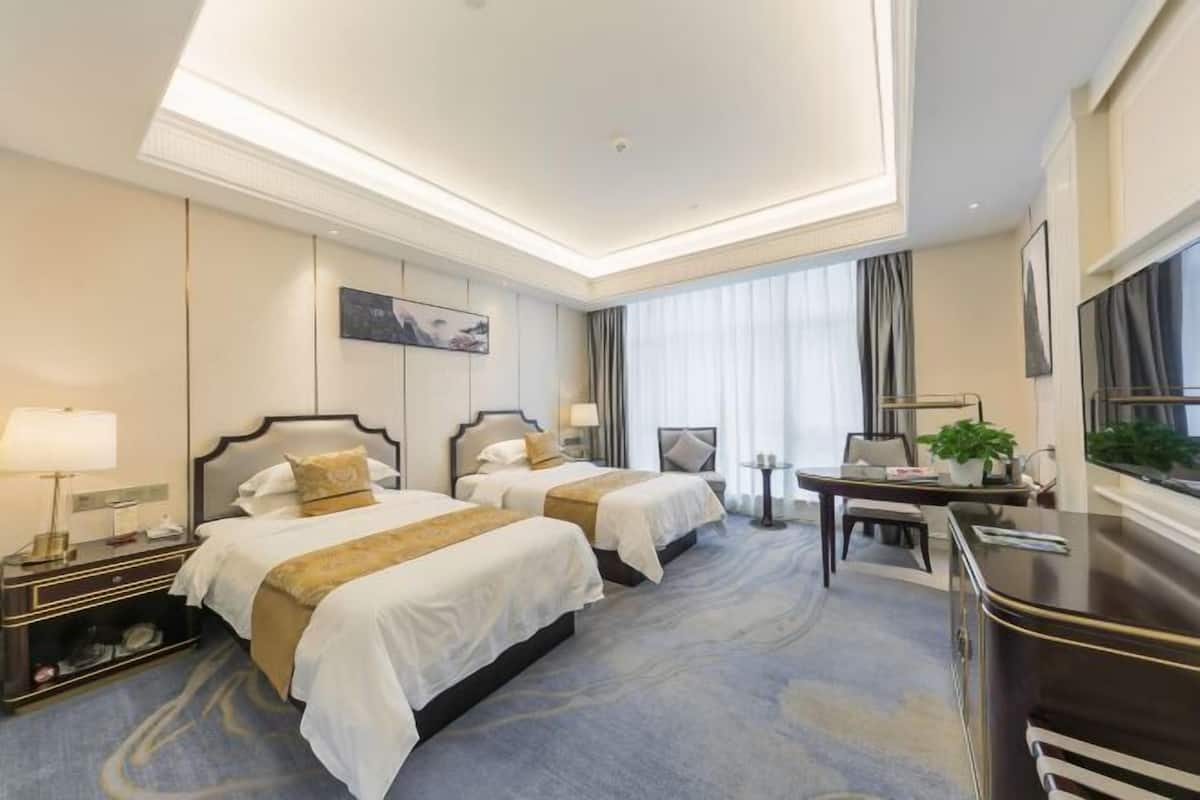 A hotel room with two beds, a desk, a chair, a TV, and a window with curtains.