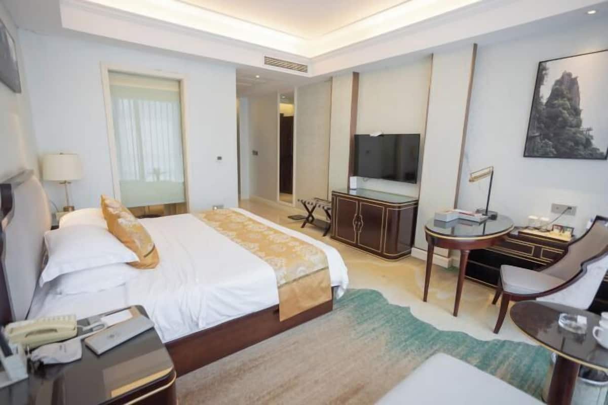 A hotel room with a large bed, a desk, a chair, a TV, and a mirror.