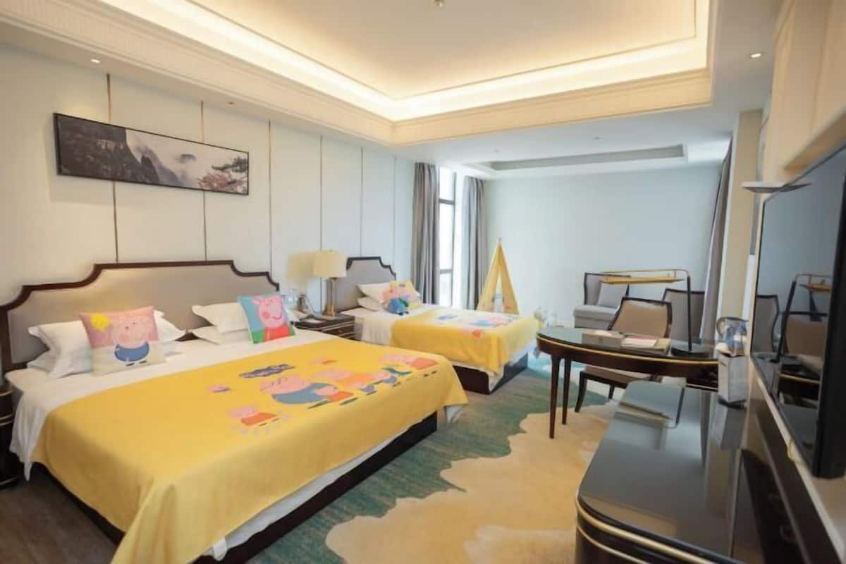 A hotel room with two beds, a desk, a chair, a TV, and a painting on the wall.