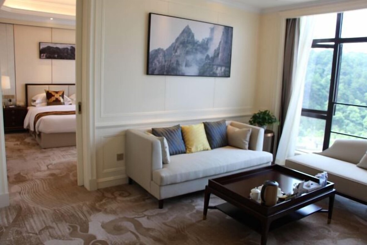 Habitación de hotel con sofá, mesa de centro, cama y un amplio ventanal con vistas al exterior.