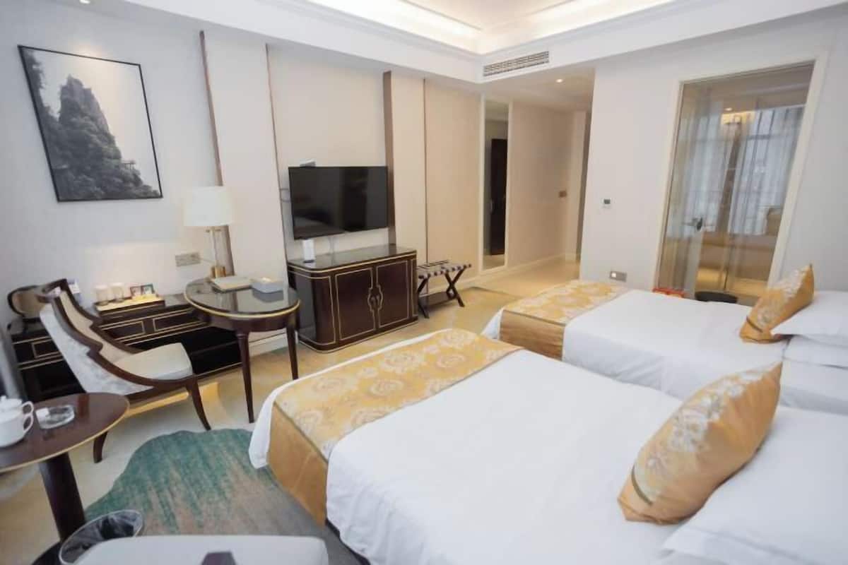 A hotel room with two beds, a TV, a desk, and a chair.