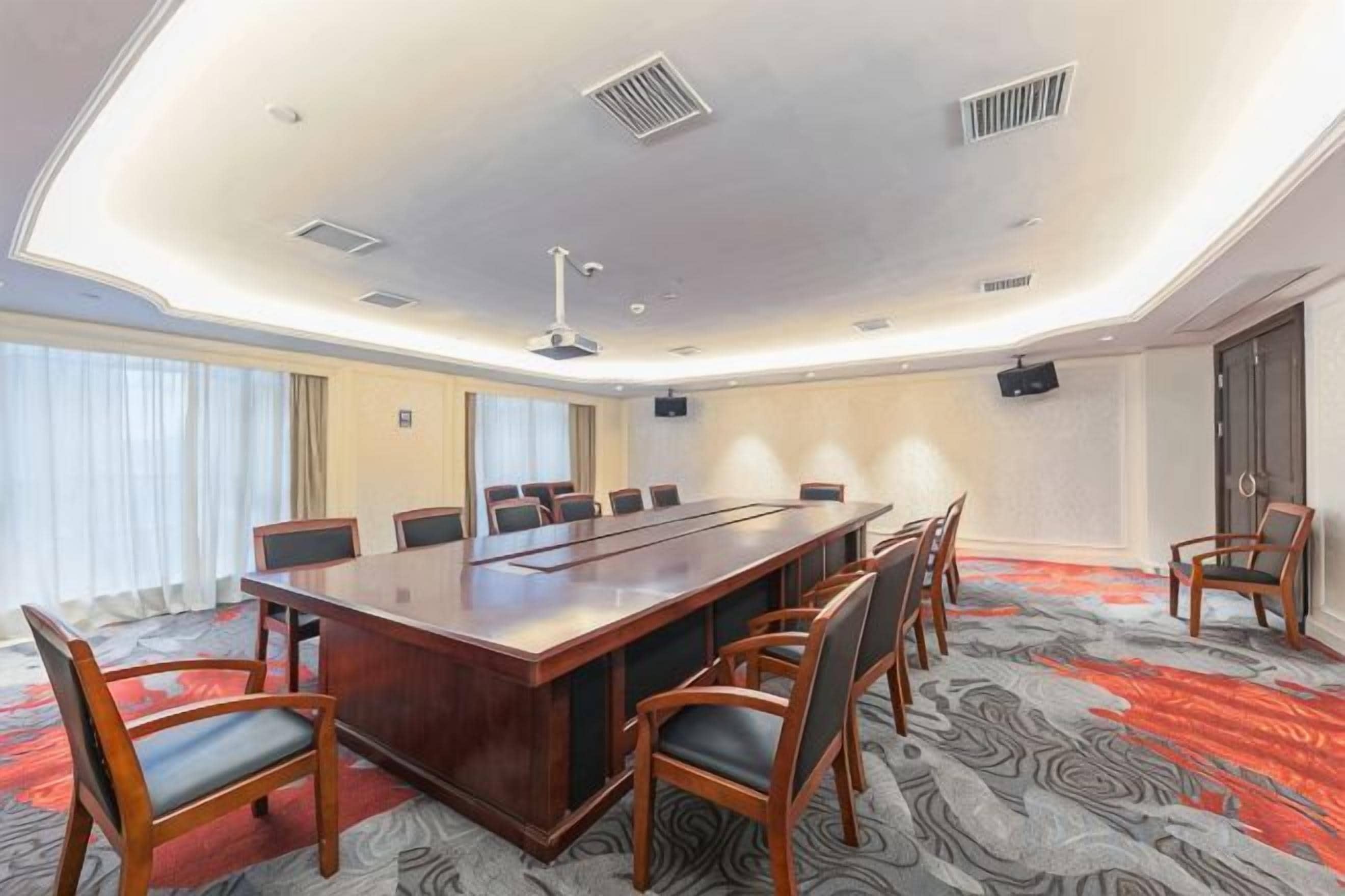 Une salle de conférence avec une longue table, des chaises, un sol recouvert de moquette et une grande fenêtre.