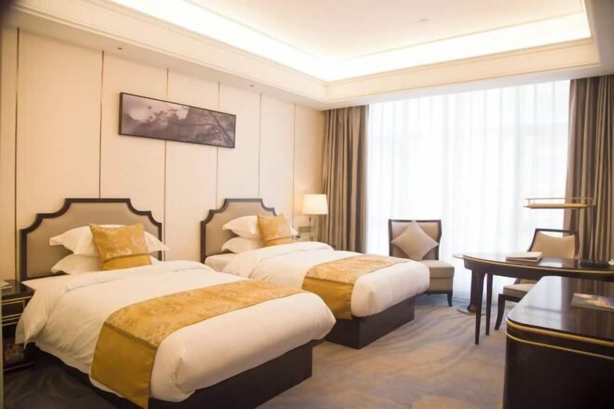A hotel room with two beds, a desk, a chair, and a large window with curtains.