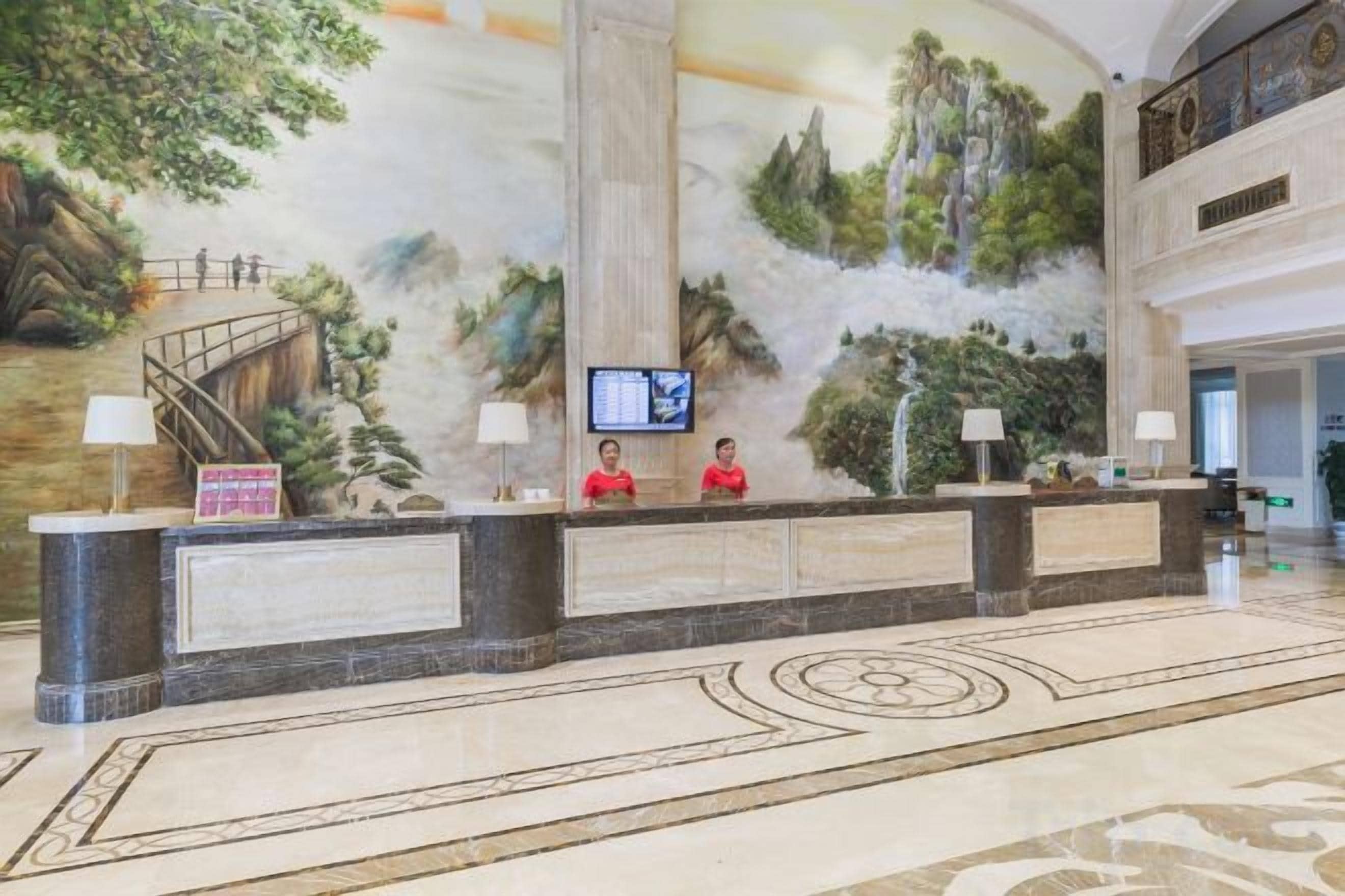 Un hall d’accueil d’hôtel avec une fresque murale, un comptoir d’accueil et un écran de télévision.