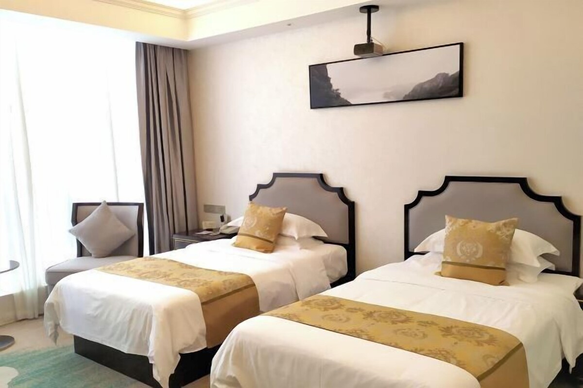Habitación de hotel con dos camas, una mesita de noche, una silla y un cuadro en la pared.