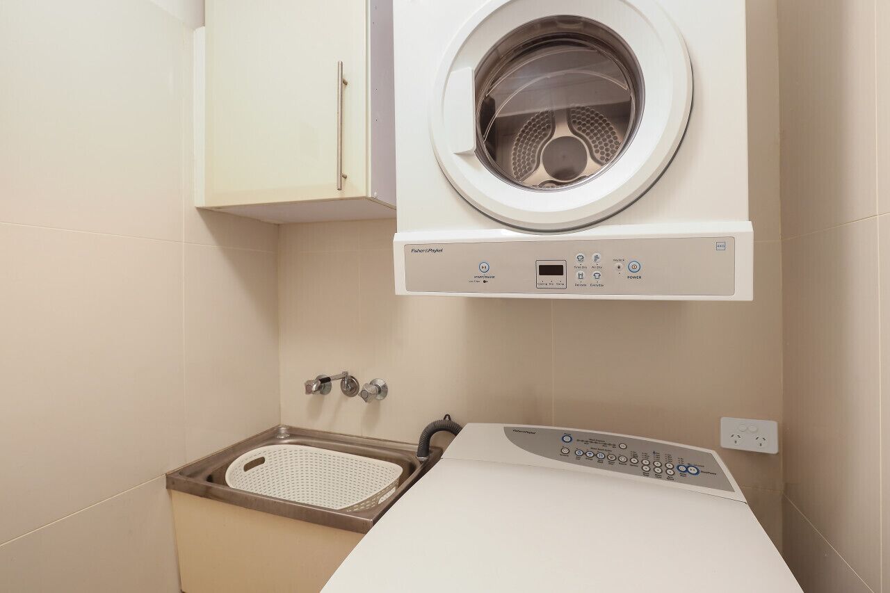Une petite buanderie équipée d’un lave-linge à chargement frontal, d’un étendoir et d’un meuble de rangement.