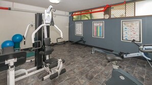 Ett gym med träningsutrustning, en väggmonterad TV och ett rött säkerhetsräcke.