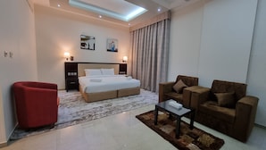 Une chambre d’hôtel moderne avec un grand lit, un fauteuil rouge, un ensemble de canapés marron, une petite table et une lucarne au plafond.