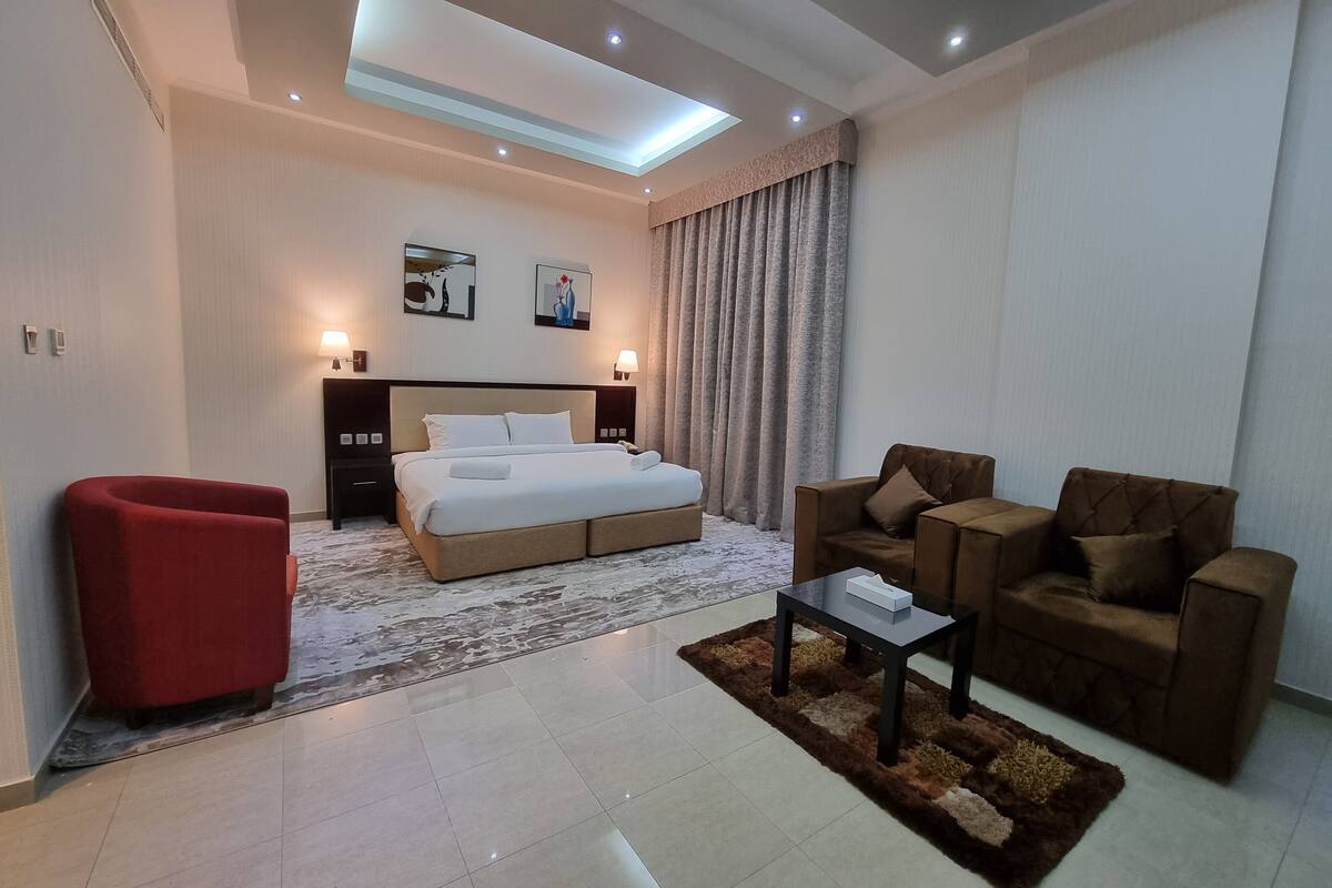 Una habitación de hotel moderna con una cama grande, un sillón rojo, un conjunto de sofá marrón, una mesita y un tragaluz en el techo.