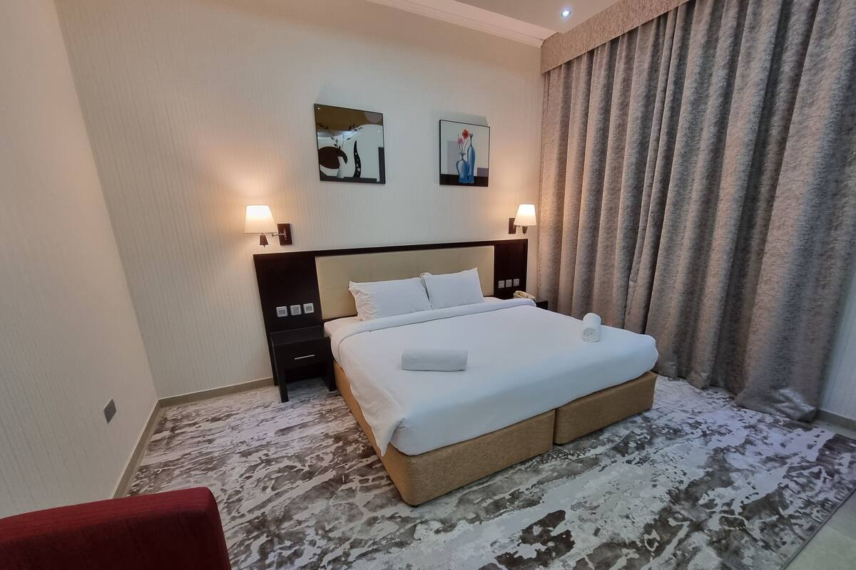 Habitación de hotel con una cama grande, dos lámparas fijadas a la pared, una mesita de noche y una silla roja.