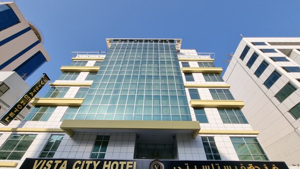 Un hôtel moderne, avec une enseigne bien visible indiquant « VISTA CITY HOTEL » et une autre dans une langue différente.